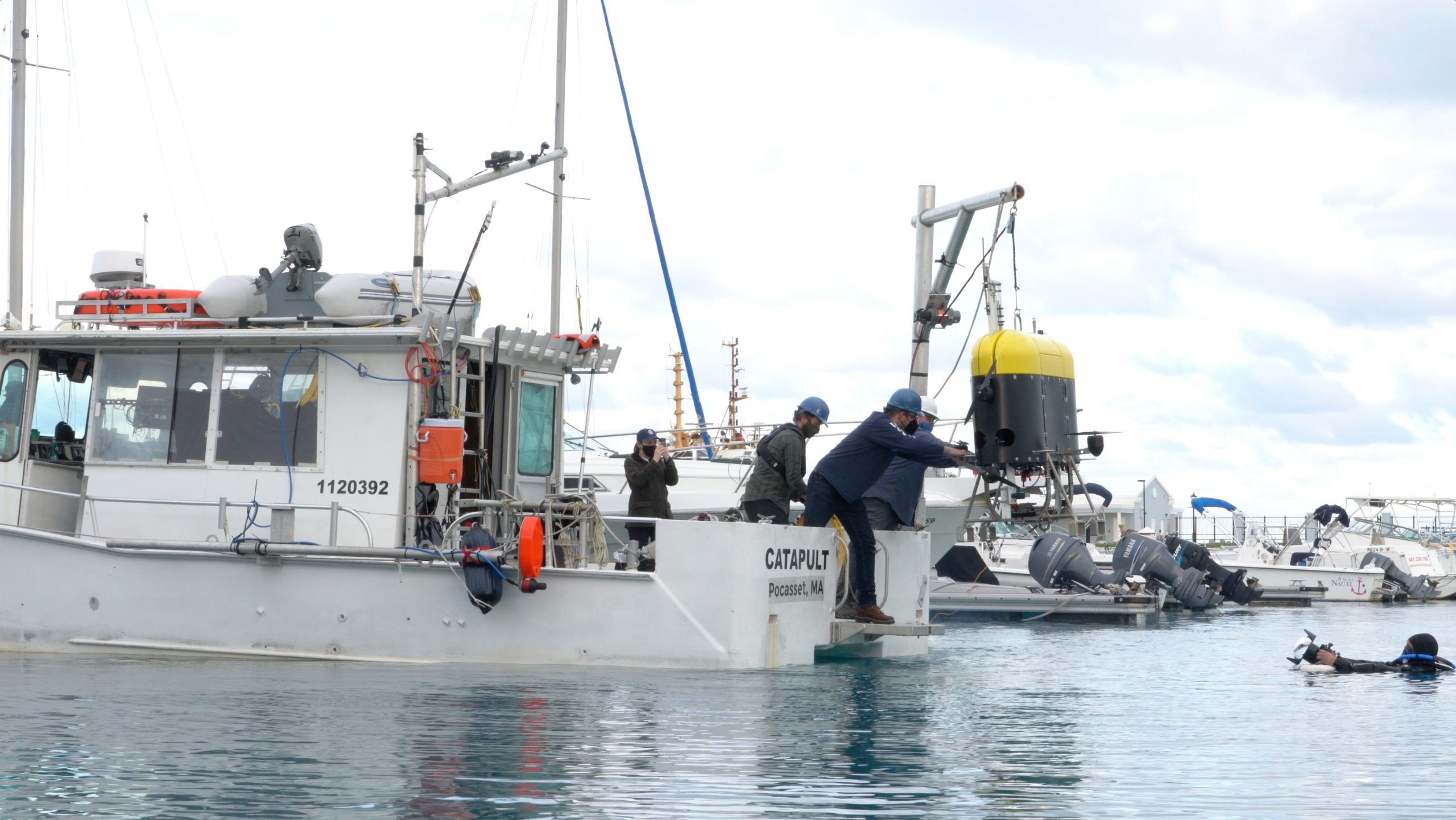 Docked at a marina, engineers Jordan Stanway and Fredrick Marin guide Mesobot into the water for testing in saltwater as engineer and underwater videographer Evan Kovacs captures the moment from the water.