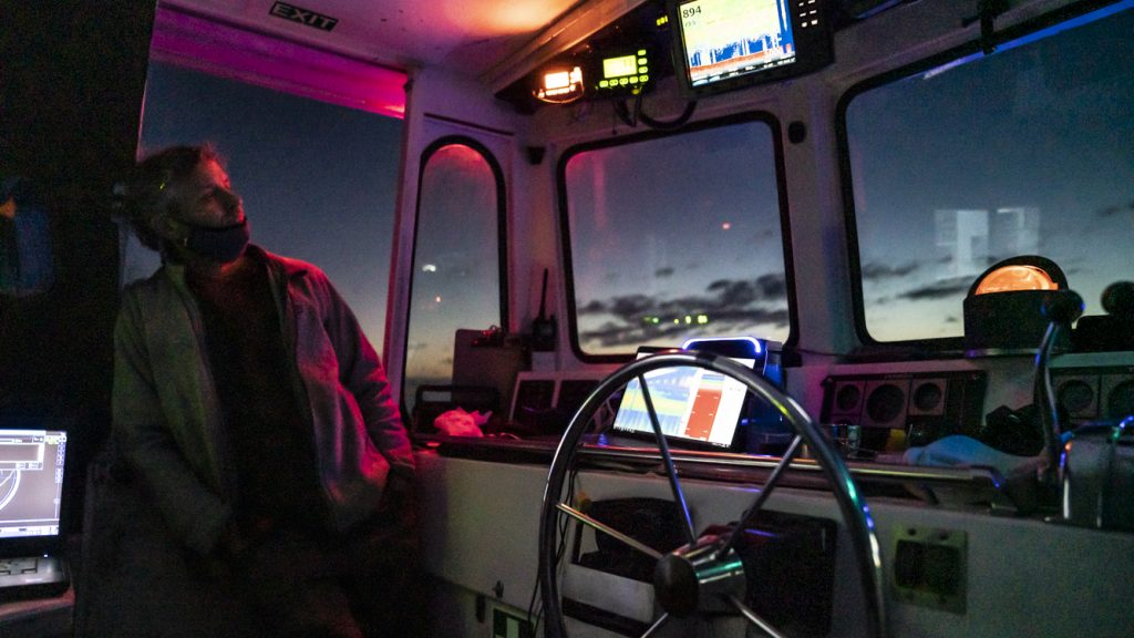 In a rare moment of calm, Evan Kovacs takes a breath to admire dusk from <em>Catapult</em>’s helm. Red lighting is used aboard the ship to limit interference from artificial light while Mesobot collects radiometer data below.
Credit: Jennifer Berglund
