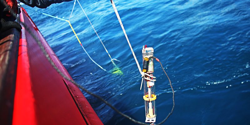 A technician lowers a MINION float over the side of the aft deck of the R/V <i>Neil Armstrong</i> in 2019.